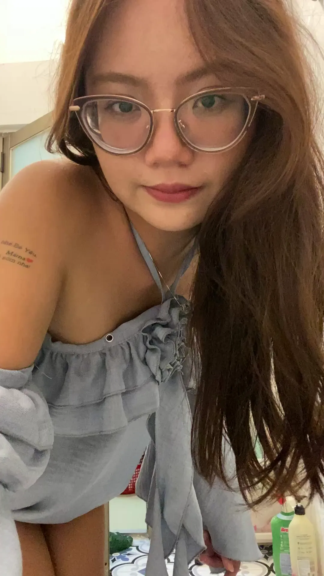 Bother_Altruistic frame at 00:00, The frame captures Bother_Altruistic's signature nerdy-sexy dichotomy: dark-framed glasses frame a coy smile while her off-the-shoulder top teases collarbones and that peekaboo shoulder tattoo