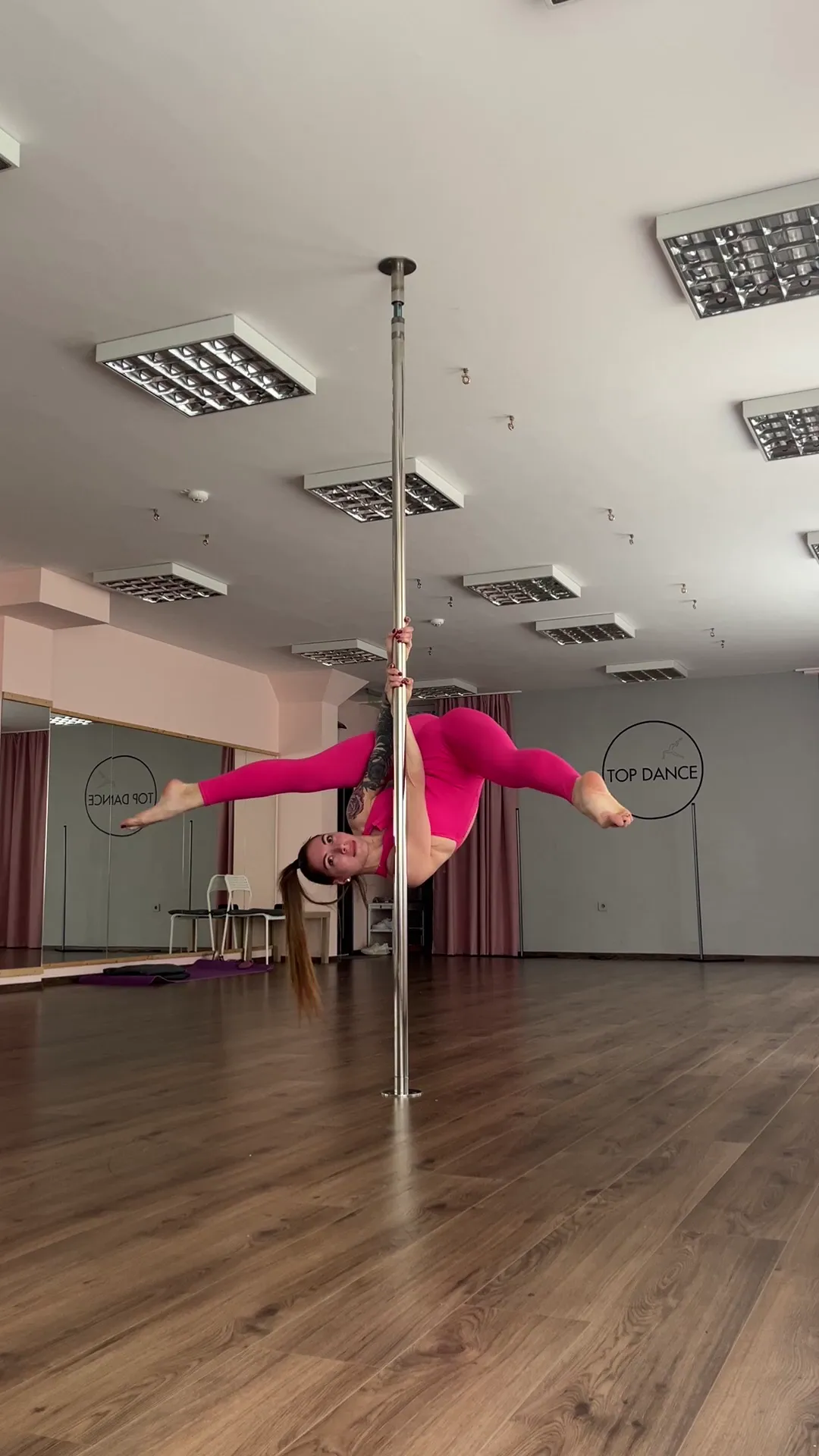 IndependentRich6963 frame at 00:24, Olivia defies gravity in this pole-dancing moment, her toned limbs and tattooed right arm flexing under studio lights