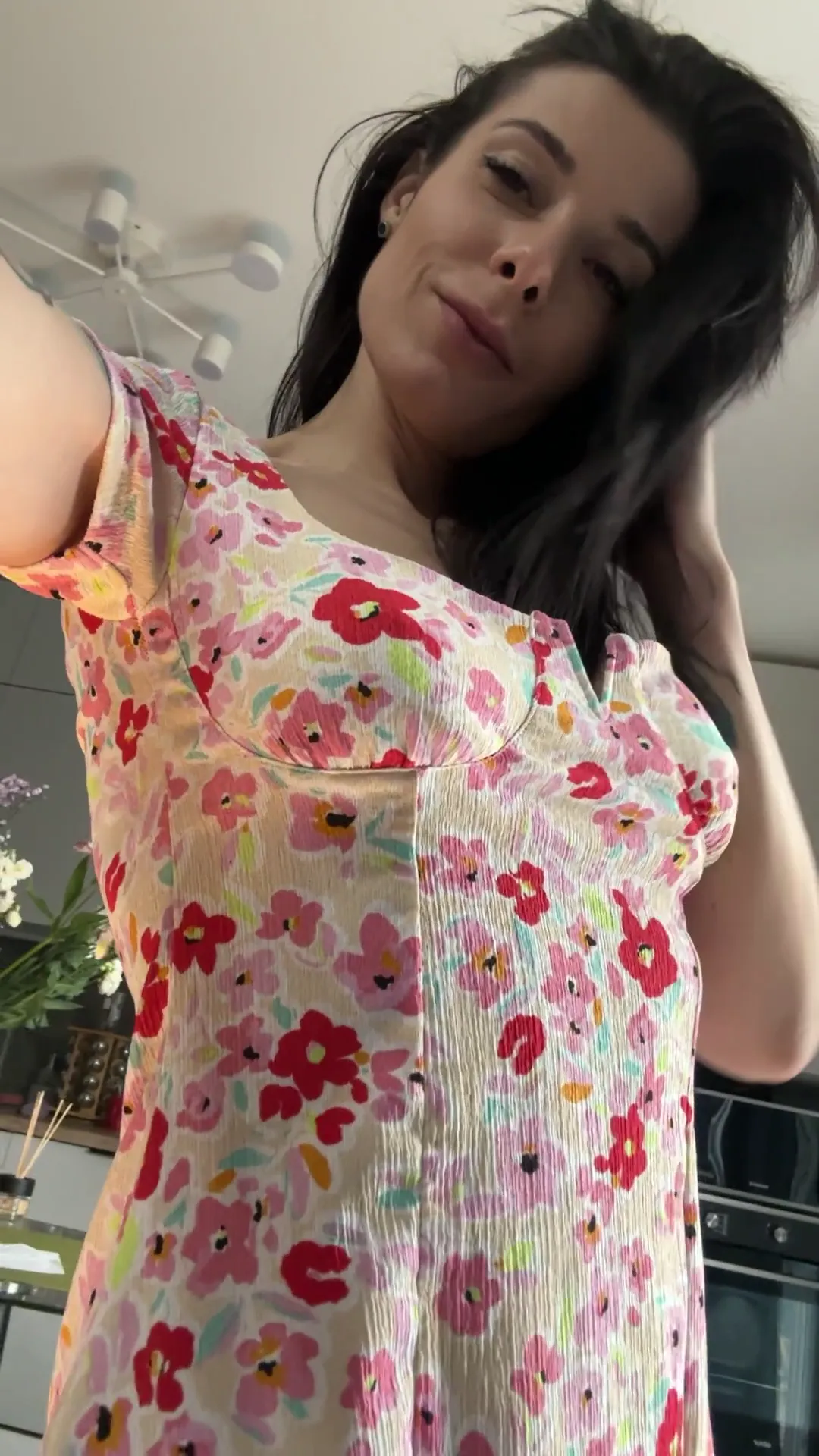 unreal_babe frame at 00:01, A deceptive slice of domesticity: unreal_babe’s floral dress and demure kitchen backdrop clash deliciously with her inked roses peeking beneath fabric and silver piercings hidden just out of frame